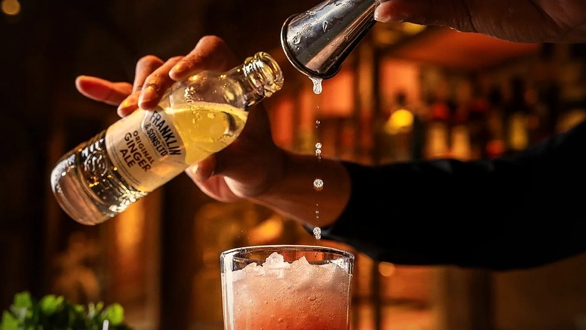 A bartender pouring a cocktail at the 709 bar, the back bar lit behind
