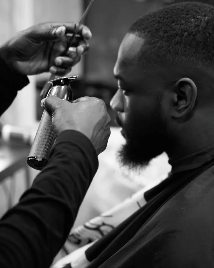 A barber shaping a fade with clippers, photographed in black and white