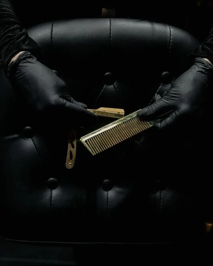 Black-gloved hands lifting a gold comb from the barber's tray