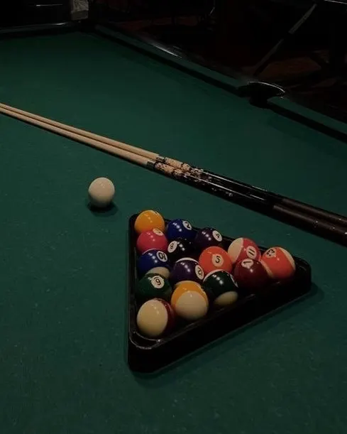 The lounge's pool table in low light, balls racked and the cue resting